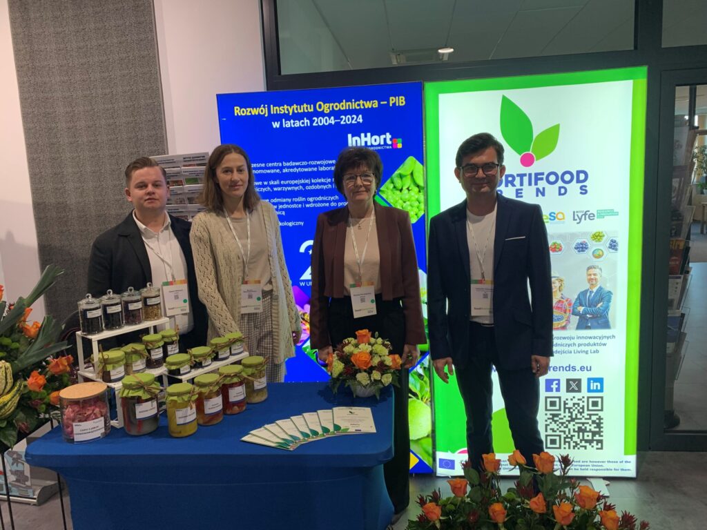 Group photo of four individuals at the HortiFood Trends exhibition booth, standing in front of promotional banners and a table with artisanal preserves and informational materials.