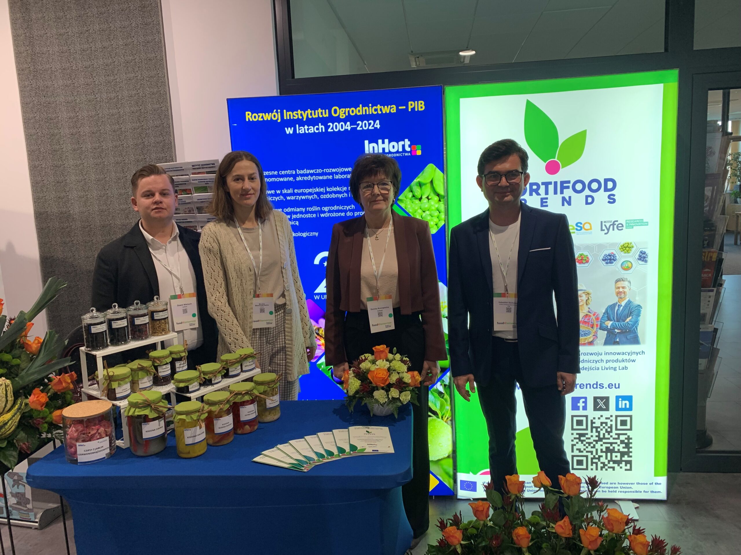 Group photo of four individuals at the HortiFood Trends exhibition booth, standing in front of promotional banners and a table with artisanal preserves and informational materials.