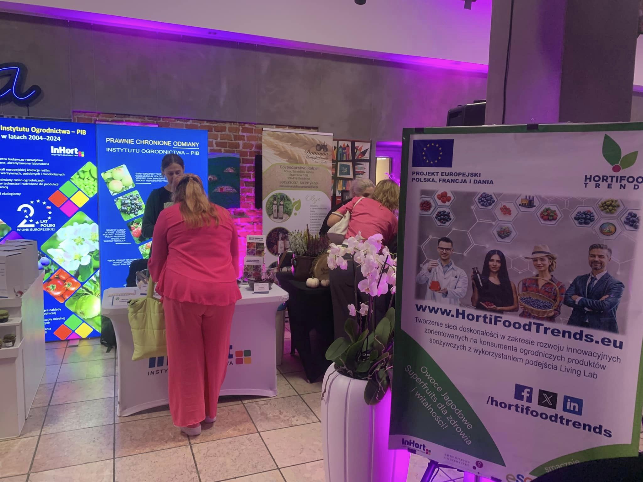 Exhibition booth showcasing HortiFood Trends promotional banner and materials, with visitors engaging at nearby displays under vibrant purple lighting.